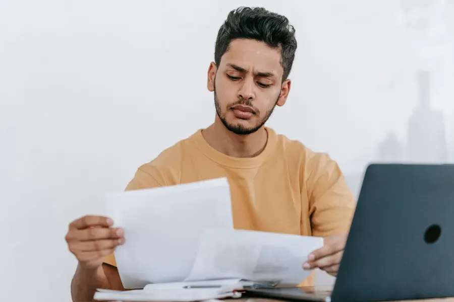 Man comparing printed documents beside a laptop