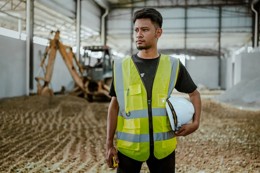 Worker in a safety vest holding a hard hat in a materials warehouse