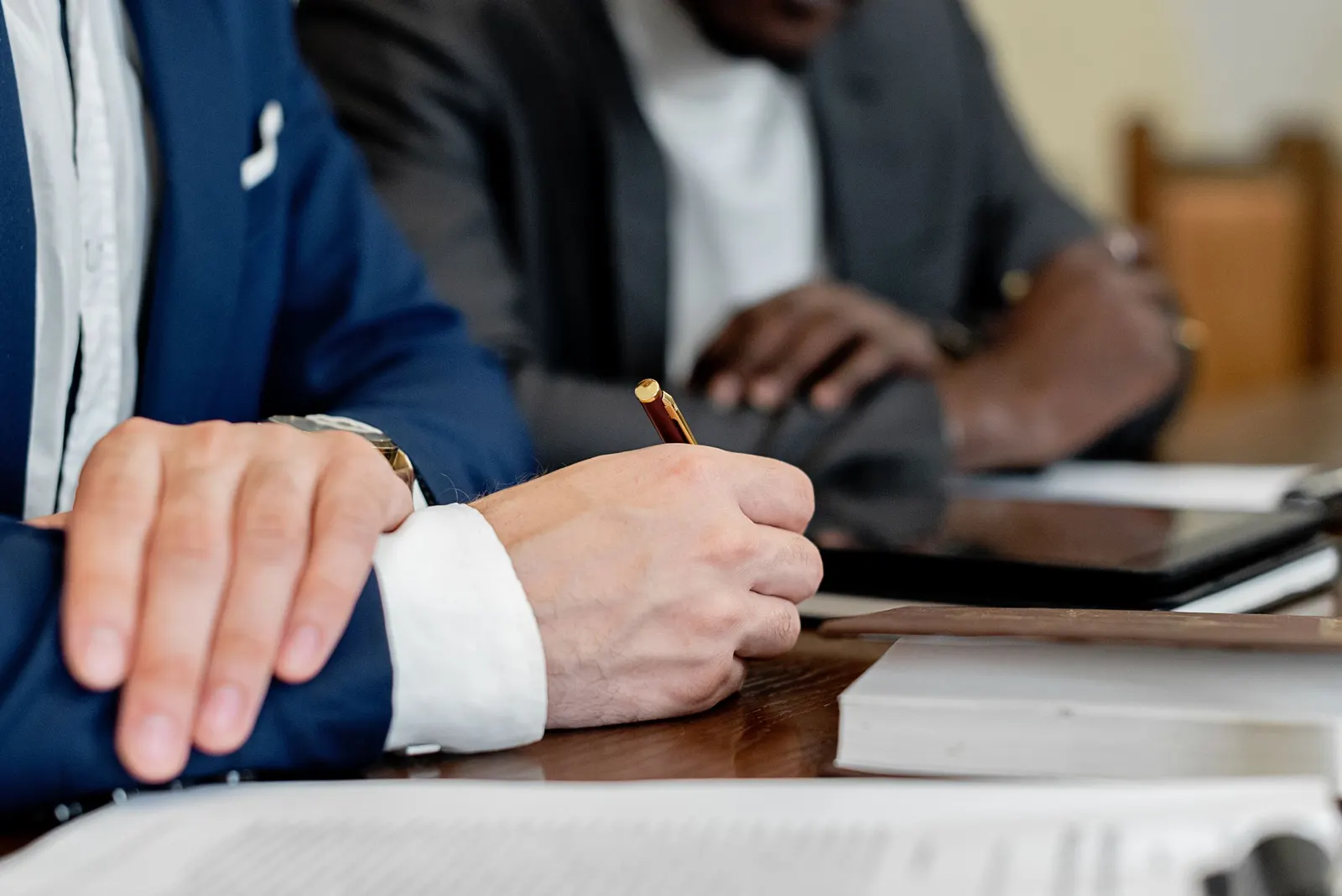 Hands writing on documents at a meeting table
